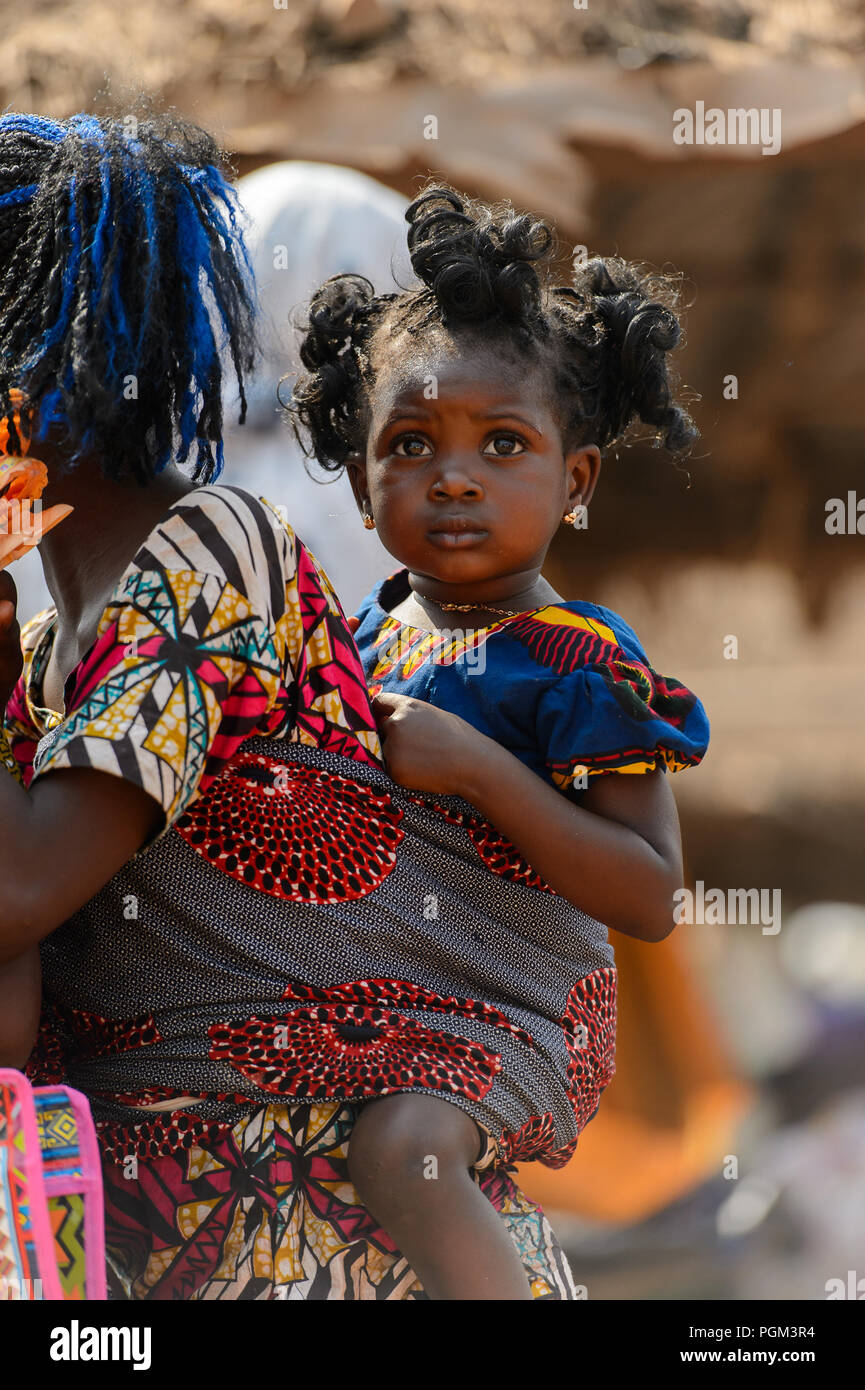 BOHICON, BÉNIN - Jan 12, 2017 : petite fille curly béninois non identifiés est porté par sa mère sur le marché local. Bénin enfants souffrent de la pauvreté Banque D'Images