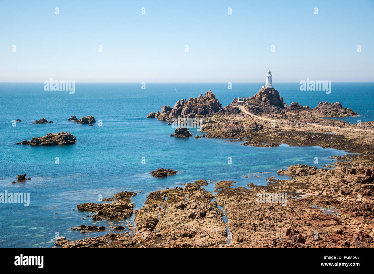 Image paysage de la Corbiere lighthouse dans le coin occidental du sud de l'île de Jersey avec des pierres au premier plan par la marée basse. Banque D'Images