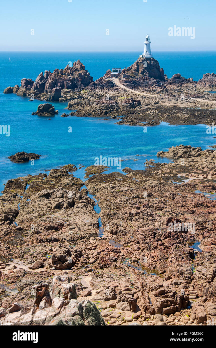 Image Portrait de la Corbiere lighthouse dans le coin occidental du sud de l'île de Jersey avec des pierres au premier plan par la marée basse. Banque D'Images