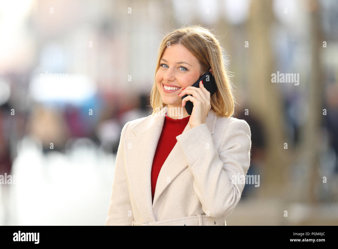 Happy woman having a phone conversation looking at camera dans la rue en hiver Banque D'Images