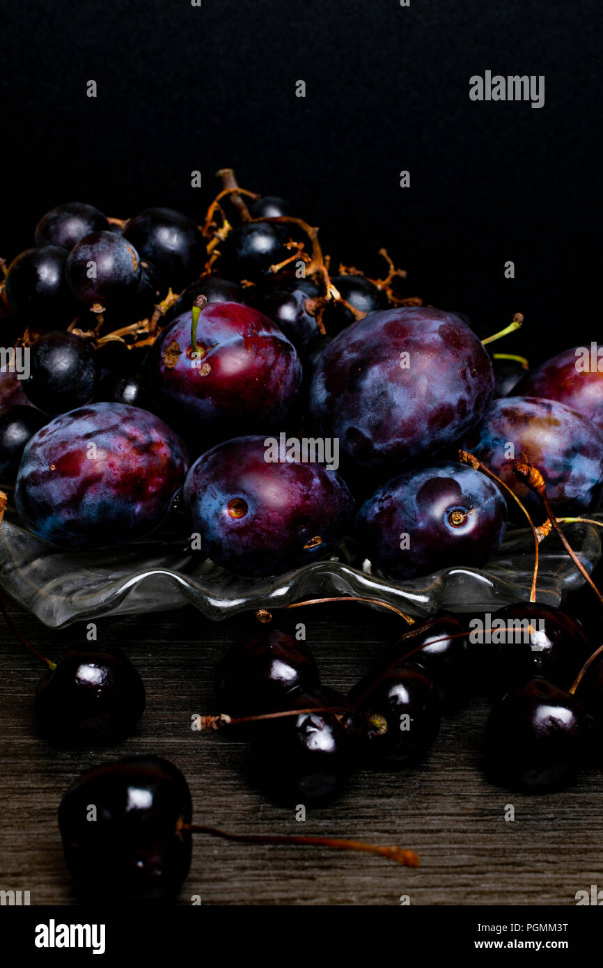 Nature morte avec raisins, prunes, cerise sur table en bois, fond noir. L'alimentation saine. Nourriture Vegan Banque D'Images
