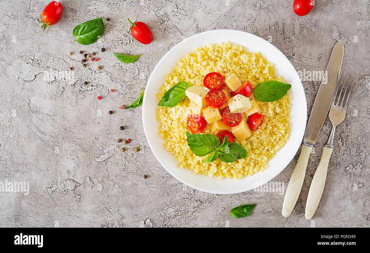 Bouillie de mil avec le fromage, le beurre et le basilic dans un bol blanc. La nourriture bonne. Le petit-déjeuner. Vue d'en haut. Mise à plat Banque D'Images