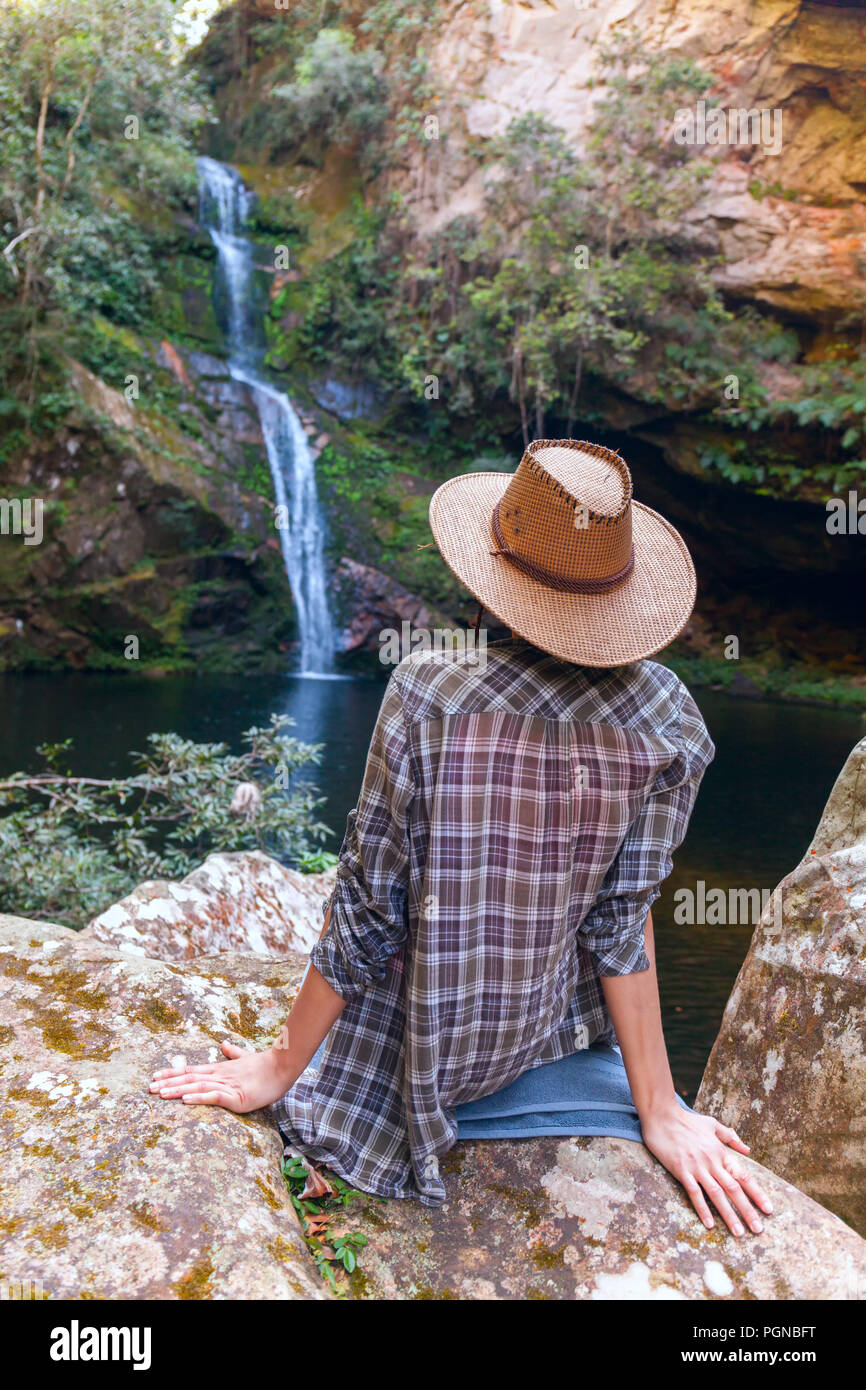 Vue arrière de jeune fille en chapeau de paille et à la recherche à cascade. Jeune femme de race blanche se penche sur la chute de l'eau, photo sur l'air frais. jeunes adolesce dans la nature sauvage Banque D'Images