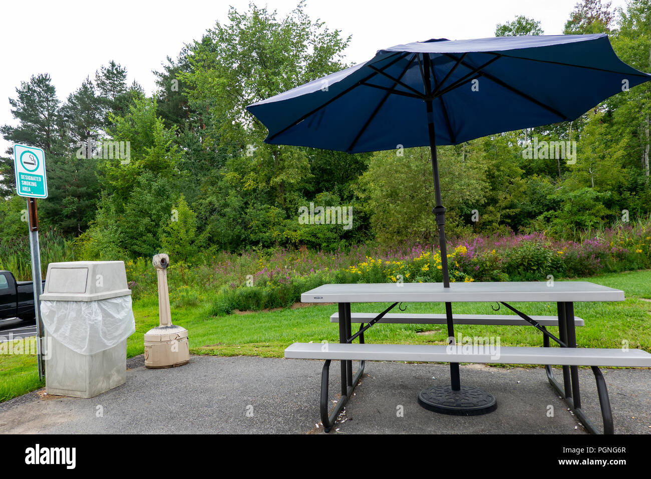 Une piscine espace fumeurs près d'un bâtiment à New Hartford, NY USA avec table de pique-nique, parasol, poubelle, et une collection de mégots de cigarettes. Banque D'Images