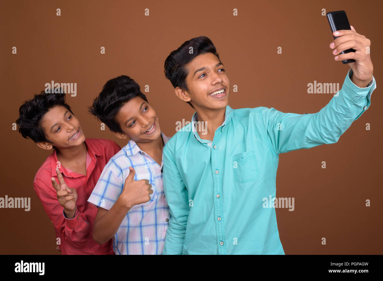 Trois jeunes frères indiens ensemble contre fond brun Banque D'Images
