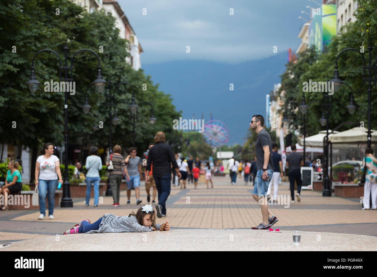 Petite fille allongée sur la rue jouant avec son smart phone, dans le centre de la zone piétonne de Sofia, Bulgarie Banque D'Images