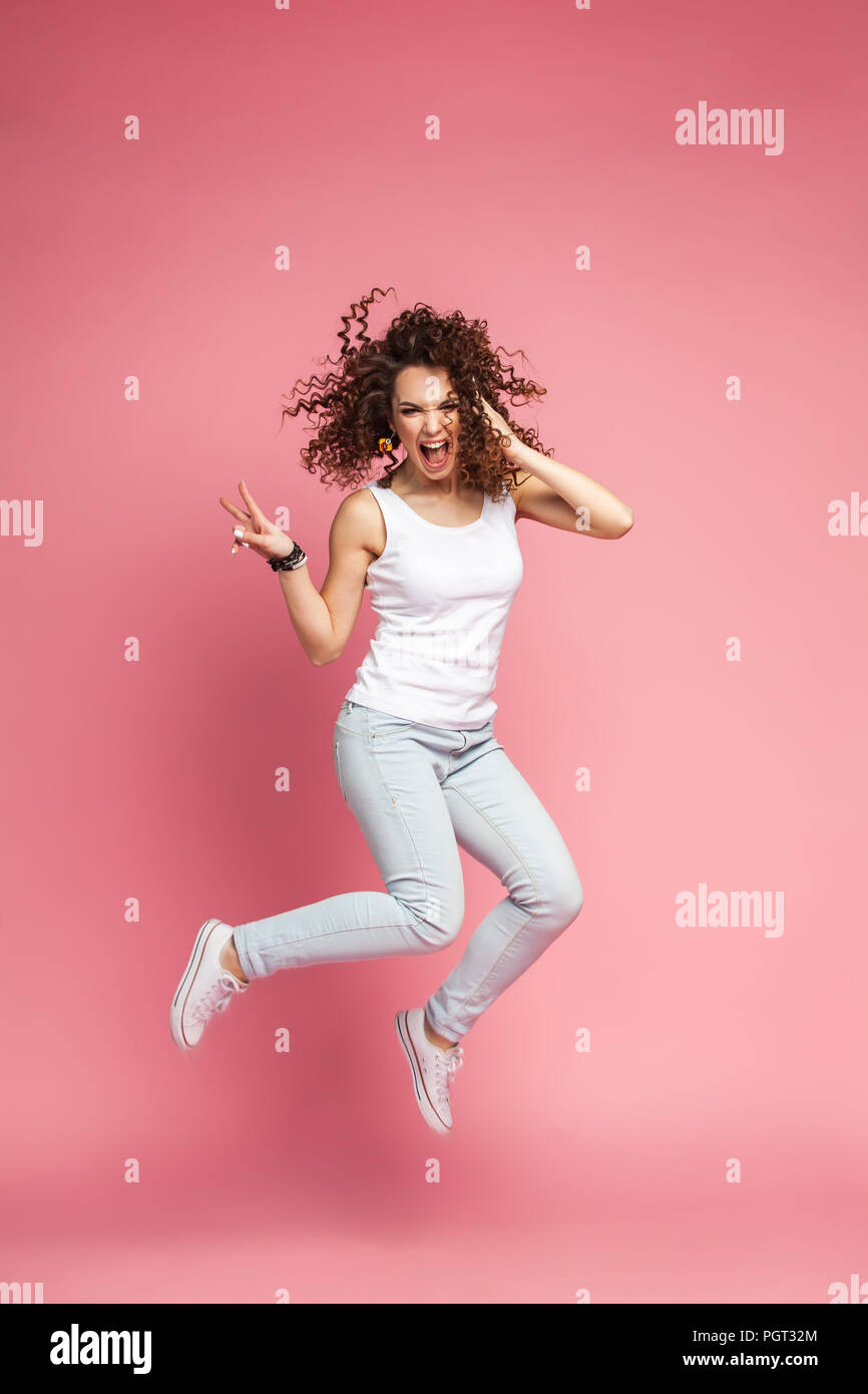 Portrait d'une jeune femme sautant de joie et célébrer plus de fond rose. Banque D'Images