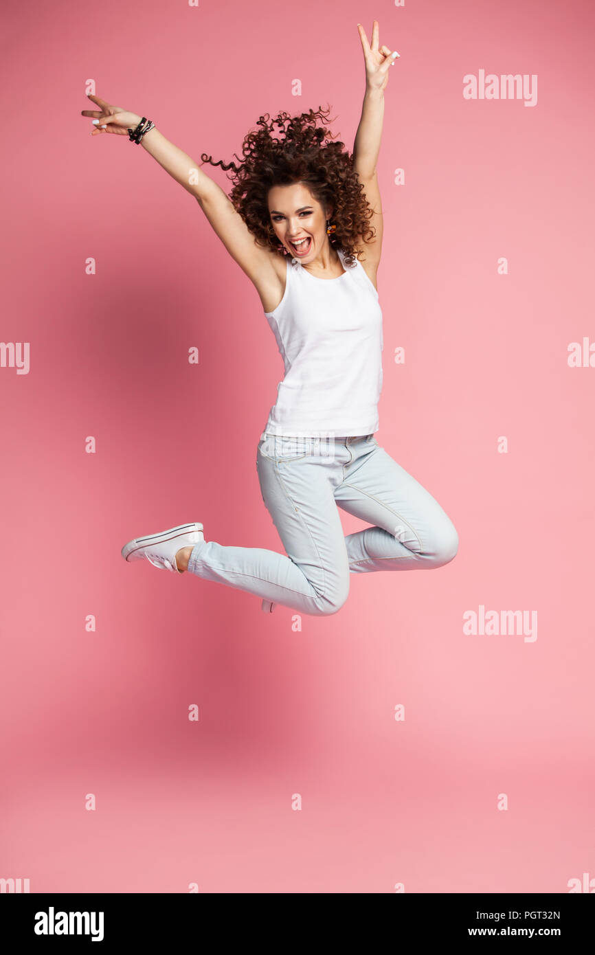Portrait d'une jeune femme sautant de joie et célébrer plus de fond rose. Banque D'Images