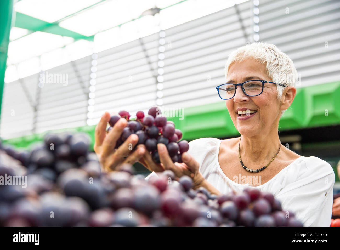 Portrait of senior femme choisit de raisins rouges au marché Banque D'Images