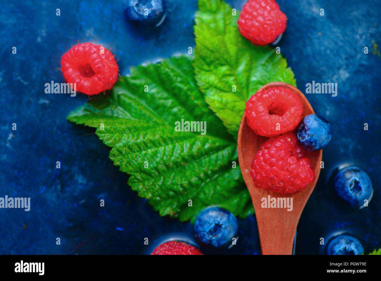 Close-up de l'été des baies en spoonsRaspberry en bois et myrtille mix sur un fond bleu foncé avec copie espace humide. En-tête de matières premières Banque D'Images
