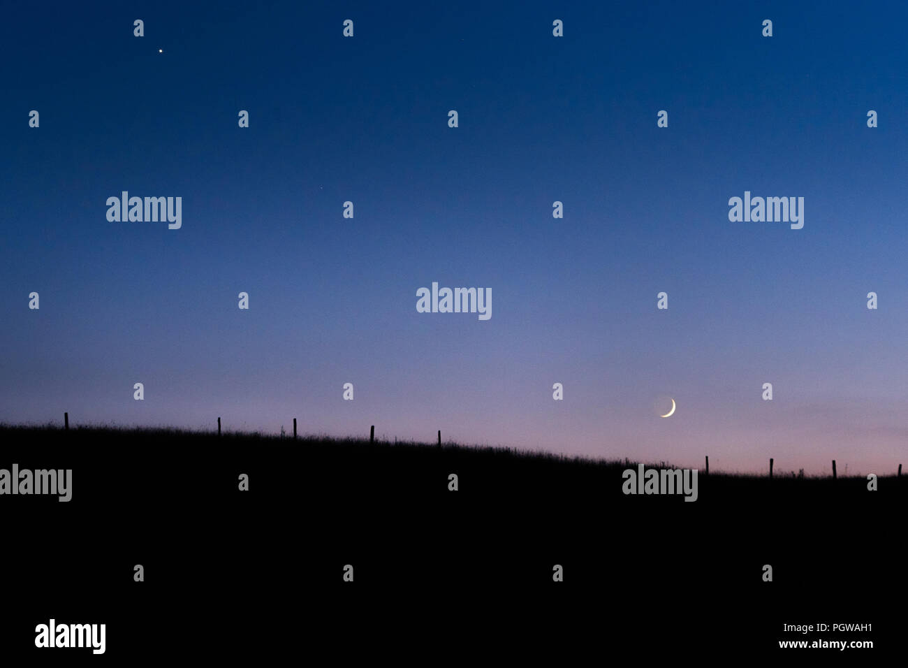 L'horizon berceaux le croissant de lune dans la pâle lueur du crépuscule pastel sous Vénus, une ancienne ligne de clôture est visible le long des douces collines. Banque D'Images