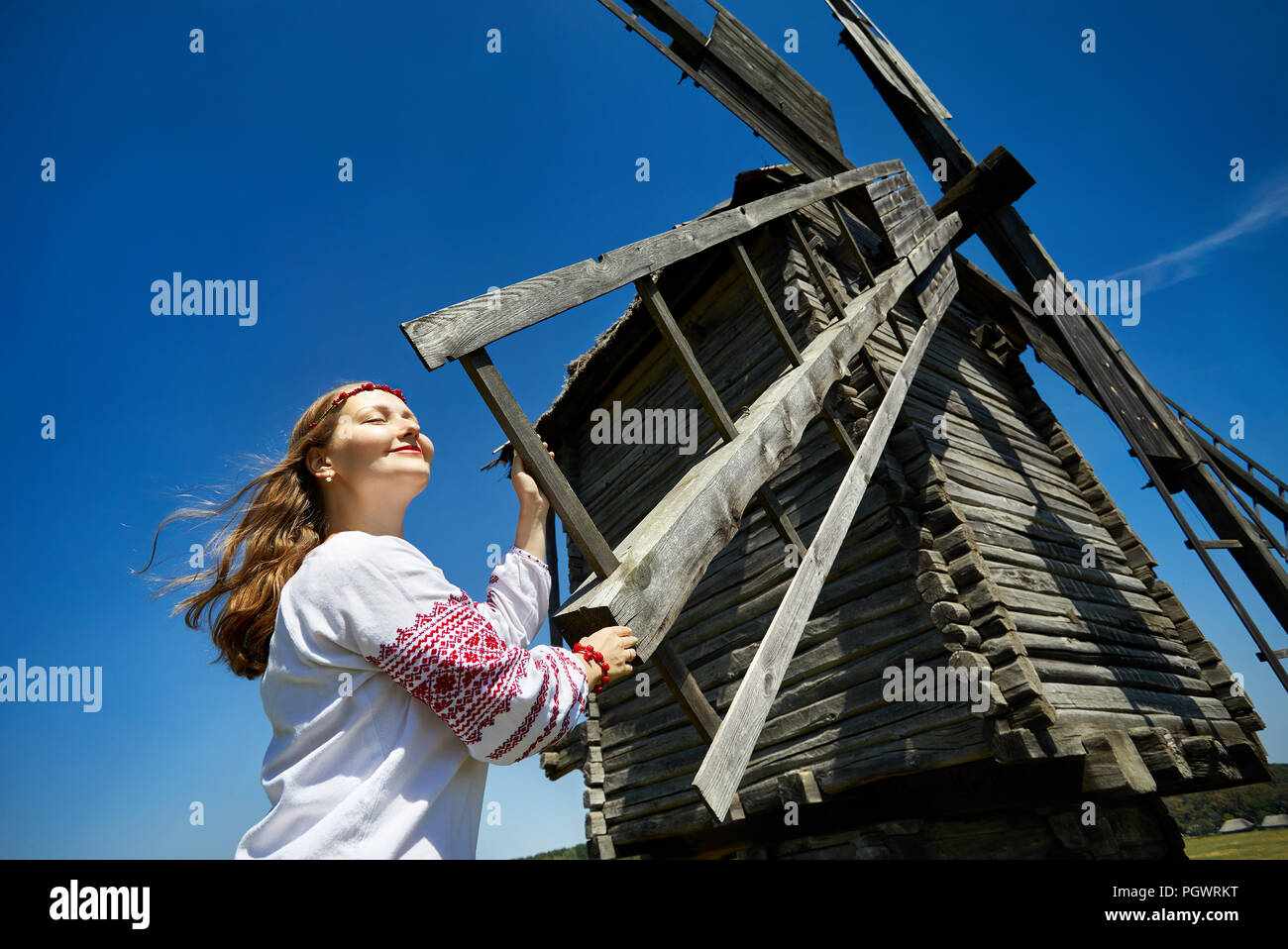 Belle jeune fille ukrainienne près de moulin à vent en bois blanc en chemise ethnique à l'architecture nationale museum à Pirogovo. Kiev, Ukraine Banque D'Images