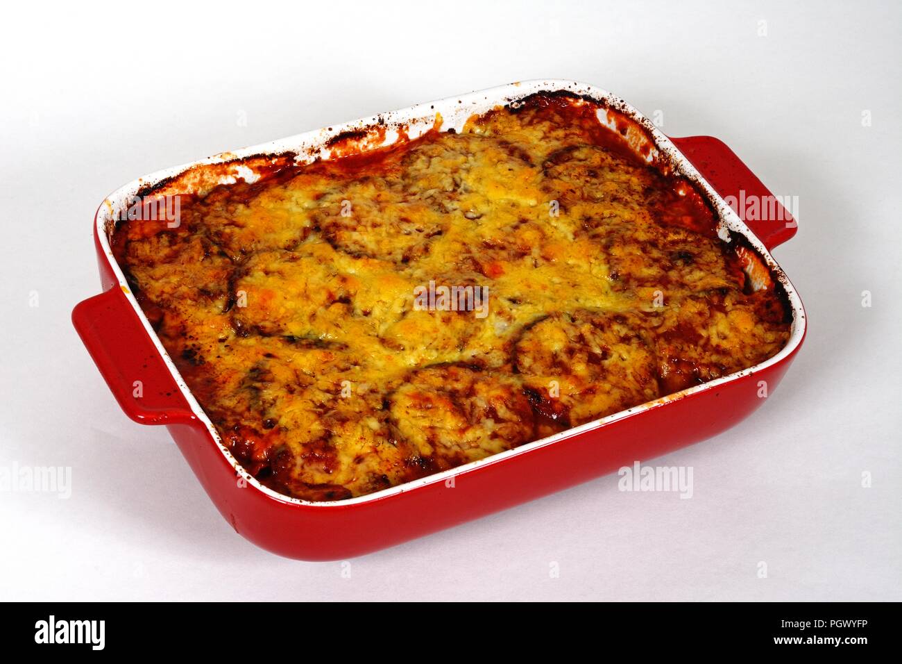 Les couches d'aubergine, tomate et fromage garni de fromage fondu dans un plat de cuisson en céramique rouge. Banque D'Images