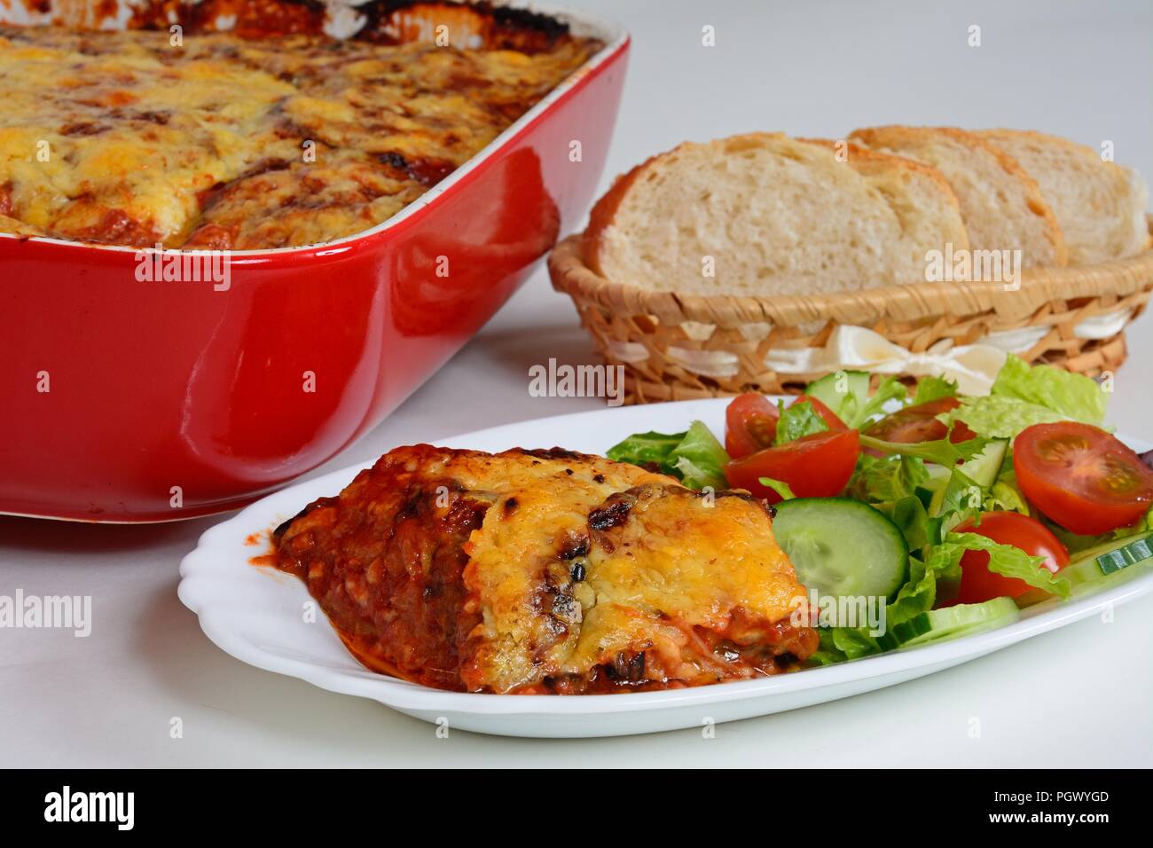 Les couches d'aubergine, tomate et fromage garni de fromage fondu servi avec de la salade et du pain avec le reste de l'aubergine cuite dans un red Banque D'Images