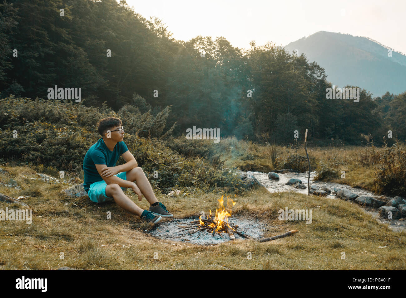 Jeune randonneur assis à côté du feu et profiter de l'ambiance du soir Banque D'Images