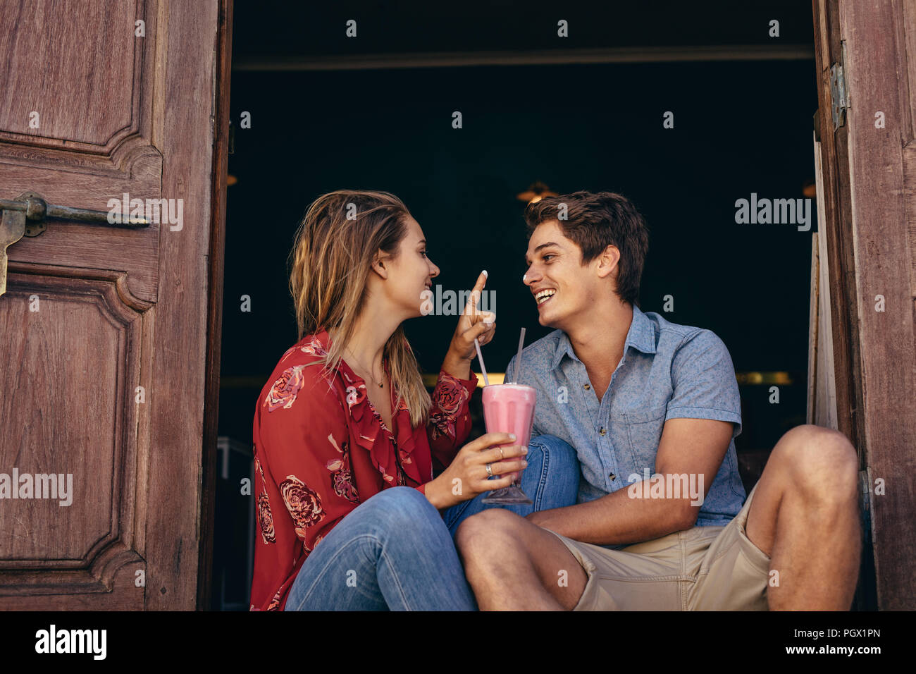 Heureux couple partageant un milkshake à deux pailles. Femme s'amusant d'appliquer de la crème sur le nez du petit ami. Banque D'Images