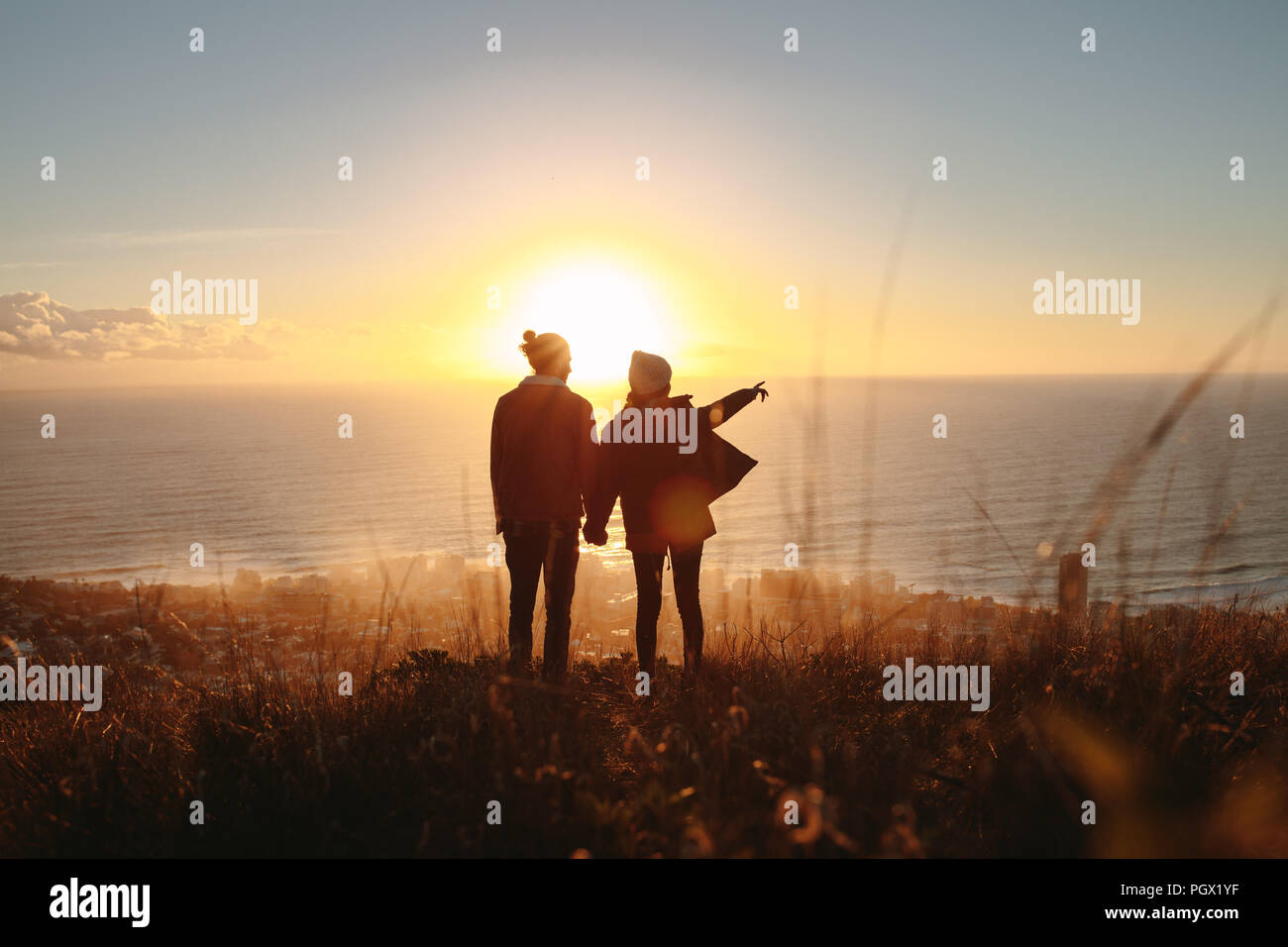 Silhouette de jeune homme et femme debout sur la montagne, avec femme opposé à la mer. Le couple marin pendant le coucher du soleil. Banque D'Images