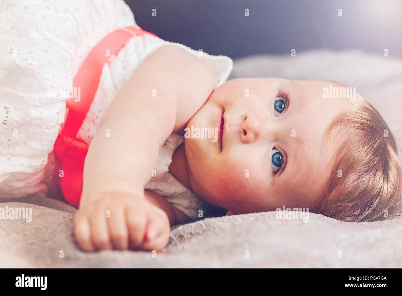 Portrait of cute adorable blonde Woman smiling baby girl l'enfant aux yeux bleus en robe blanche avec red bow lying on bed looking up dreaming, fairy Banque D'Images