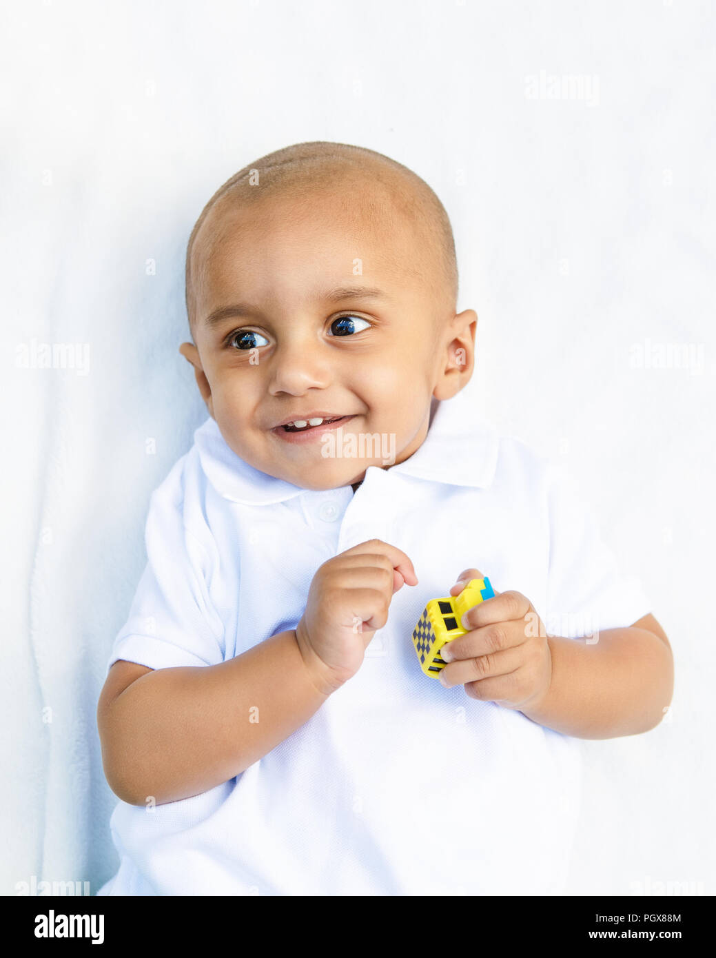 Portrait of cute adorable sourire rire little indian mixed race bébé garçon en chemise blanche sur fond blanc jouant avec jouet voiture Banque D'Images