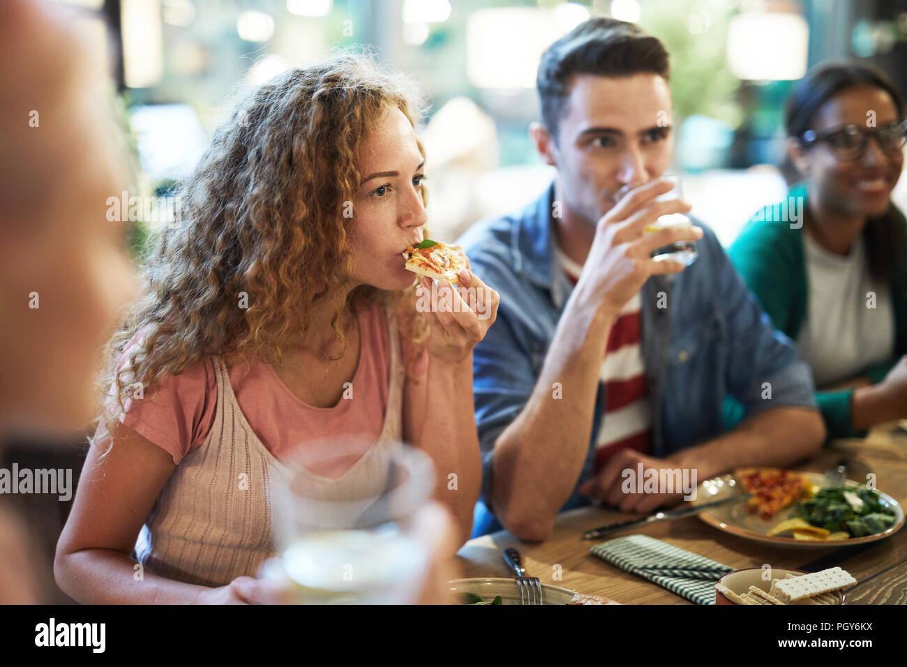 Faim casual girl eating pizza d'un dîner entre amis et à l'écoute de l'un d'entre eux au cours de chat Banque D'Images