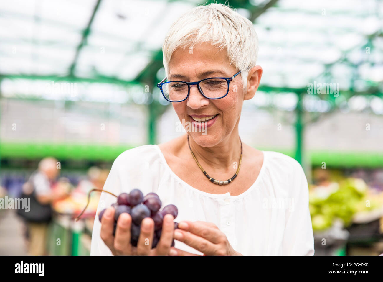 Portrait of senior femme choisit de raisins rouges au marché Banque D'Images
