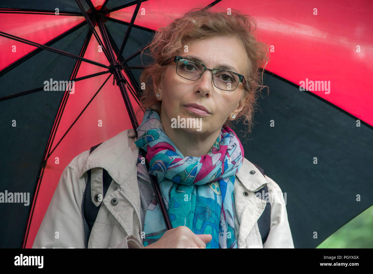 Portrait de femme d'âge moyen marche sous un parapluie rouge et noir Banque D'Images