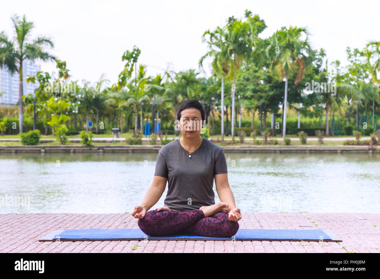 Femme asiatique d'âge moyen en bonne santé faisant du yoga lotus de poser dans les parc de la ville au matin et le mode de vie sain. concept. Banque D'Images