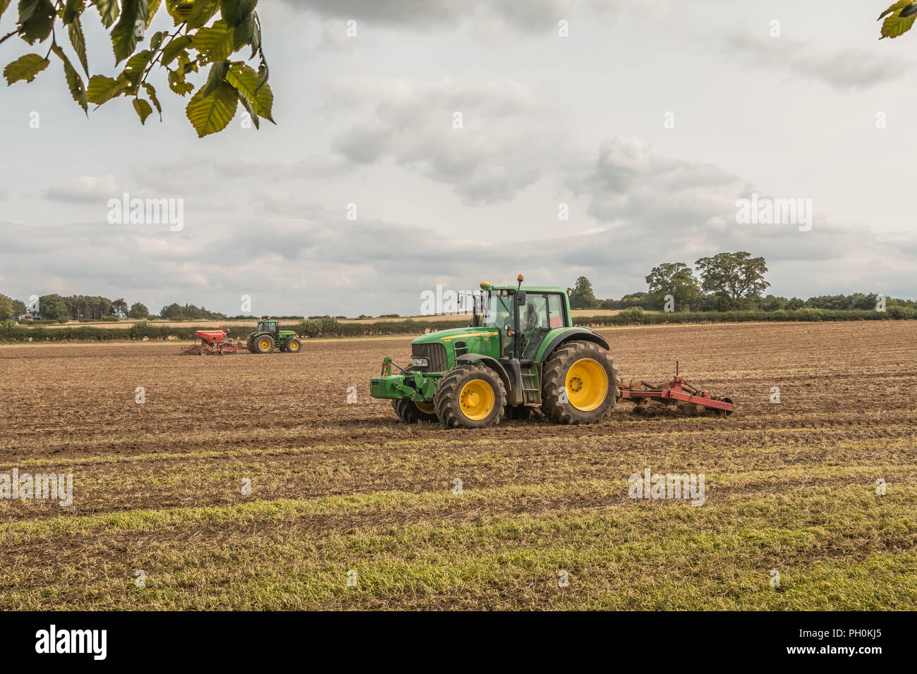 L'agriculture britannique, deux tracteurs John Deere au travail le sous-solage et semis monograine un champ moissonné Banque D'Images