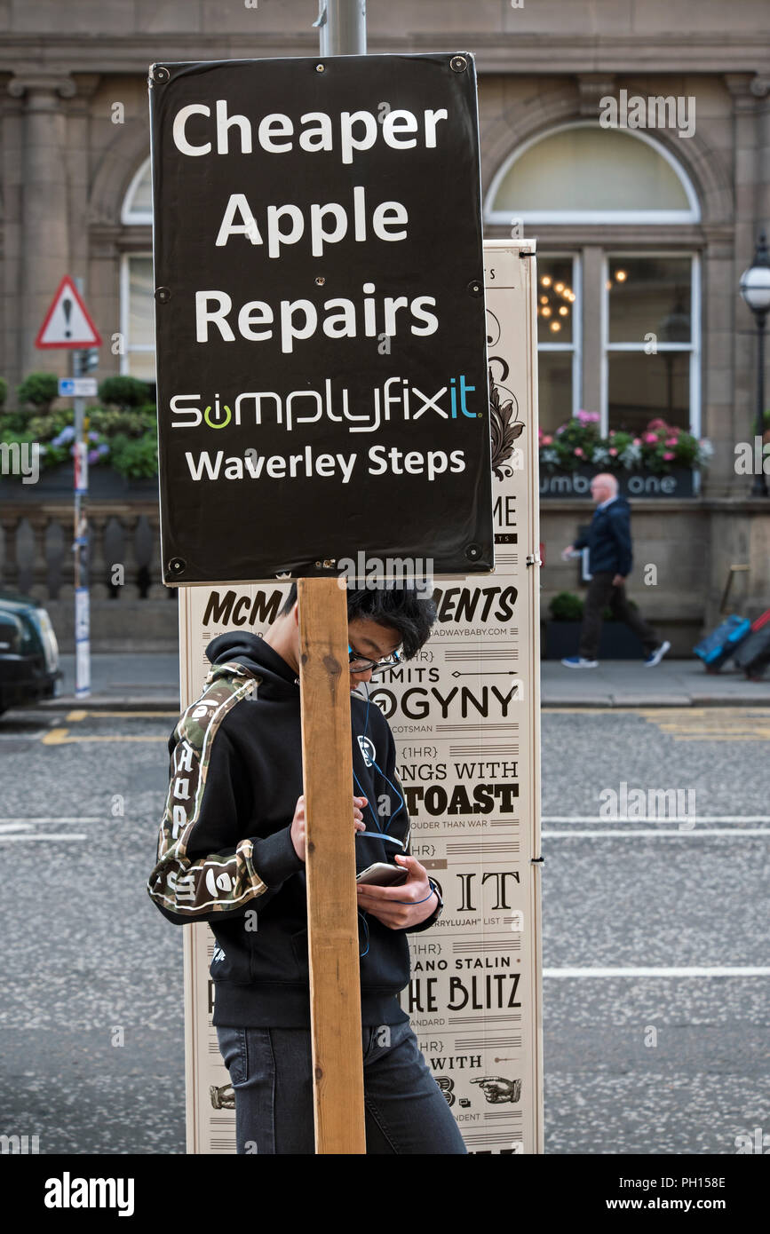 Un jeune homme vérifie son téléphone tout en maintenant une enseigne publicitaire sur Princes Street, Édimbourg, Écosse, Royaume-Uni. Banque D'Images