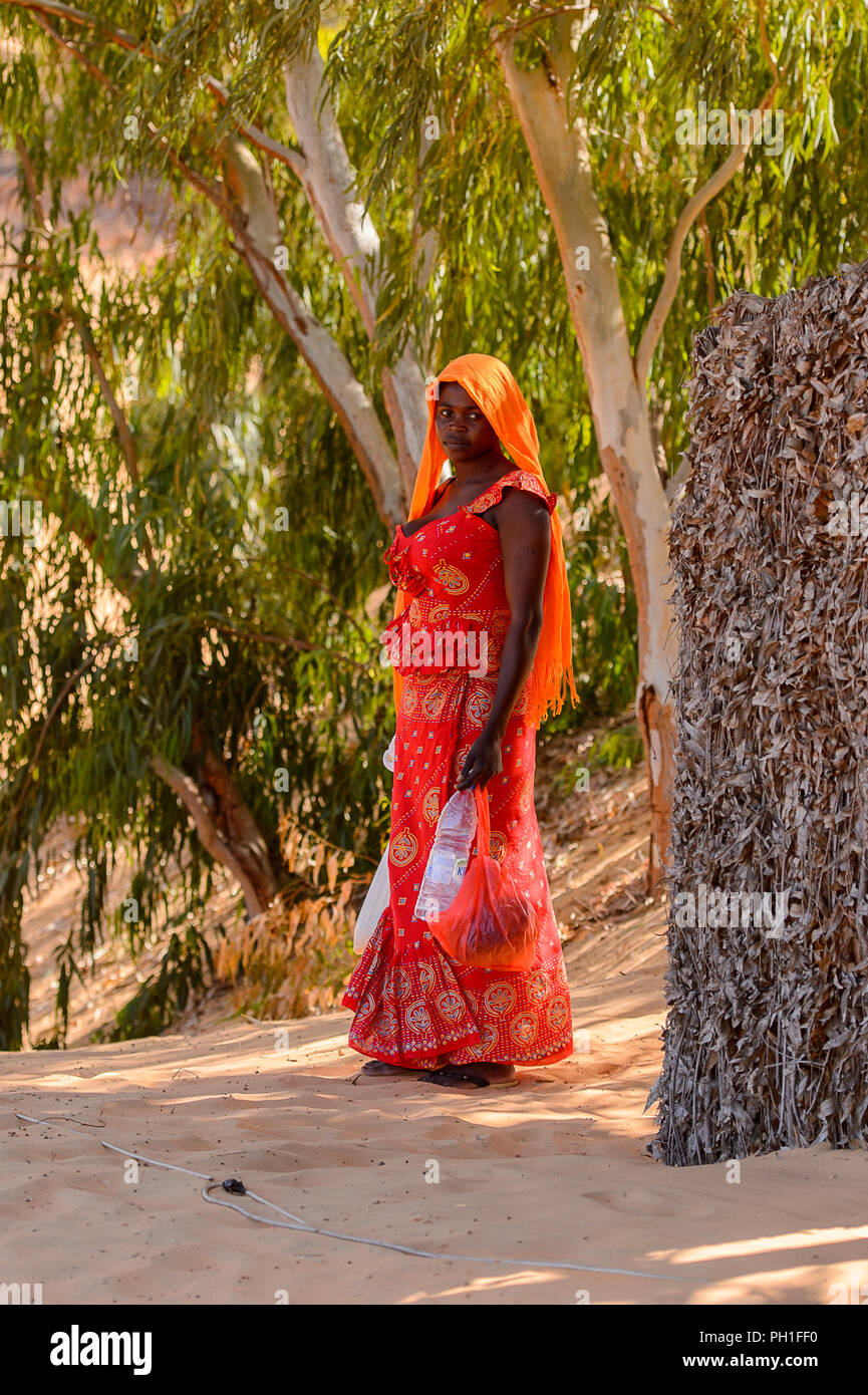 Désert de LAMPOUL, SÉNÉGAL - Apr 23, 2017 : femme sénégalaise non identifiés en rouge les vêtements traditionnels tient un sac et une bouteille d'eau dans un désert de Lampoul Banque D'Images