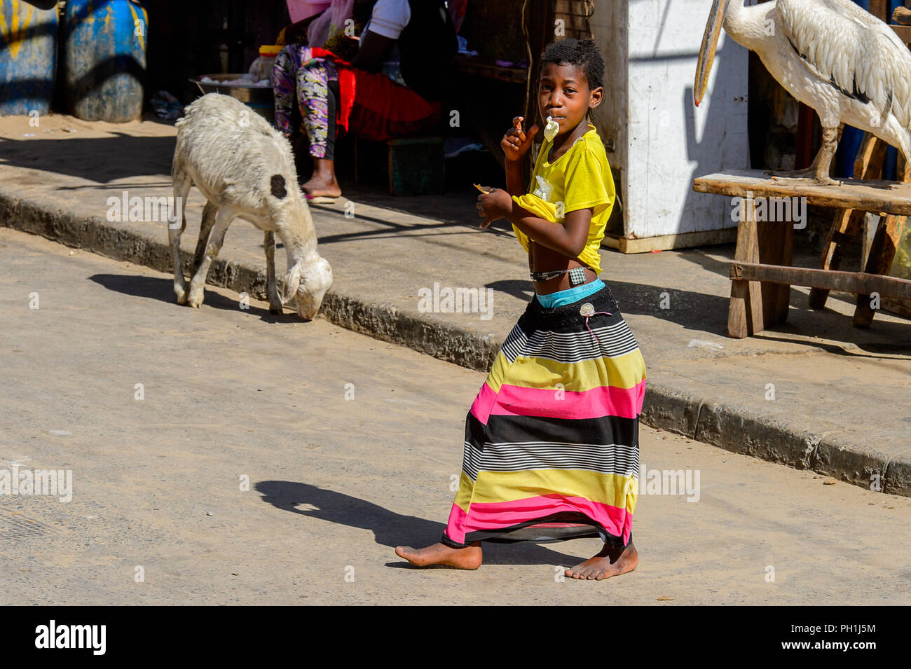 SAINT LOUIS, SÉNÉGAL - Apr 24, 2017 : fille dans sénégalais non identifiés chemise jaune jupe à rayures et mange quelque chose sur le marché local de Saint Louis, Banque D'Images