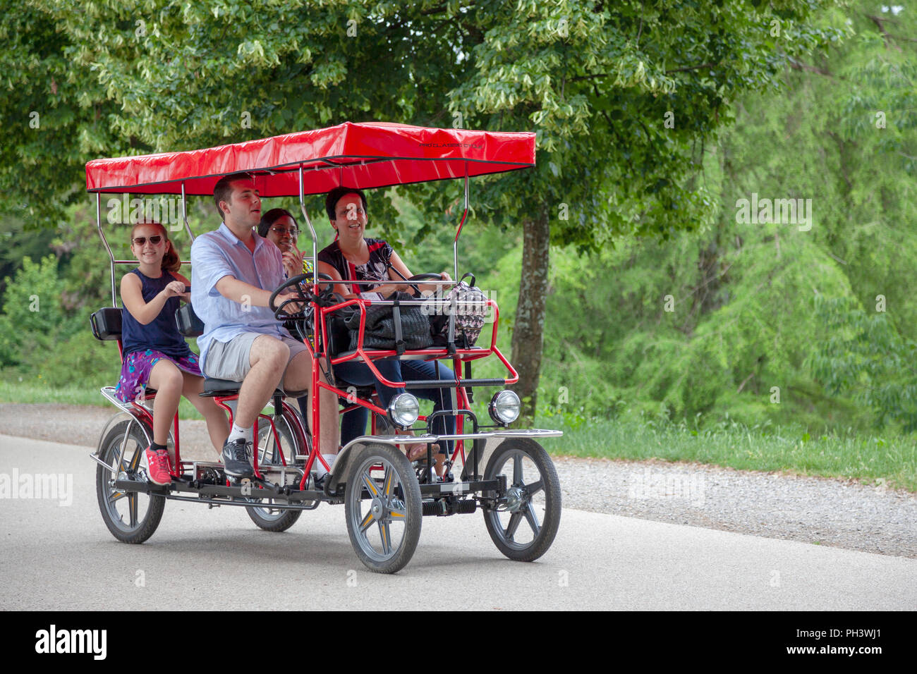 Sur les remparts de Lucques (Toscane - Italie), une famille ayant un lecteur dans une voiture à pédales à quatre roues sous l'ombre des arbres centenaires. Banque D'Images