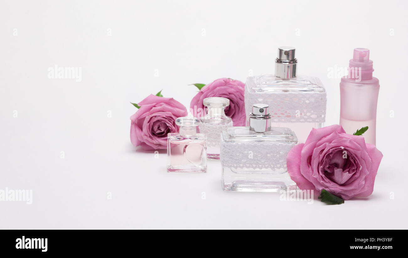Plusieurs flacons de parfum de différentes tailles avec des fleurs rose sur fond clair. Copy space Banque D'Images