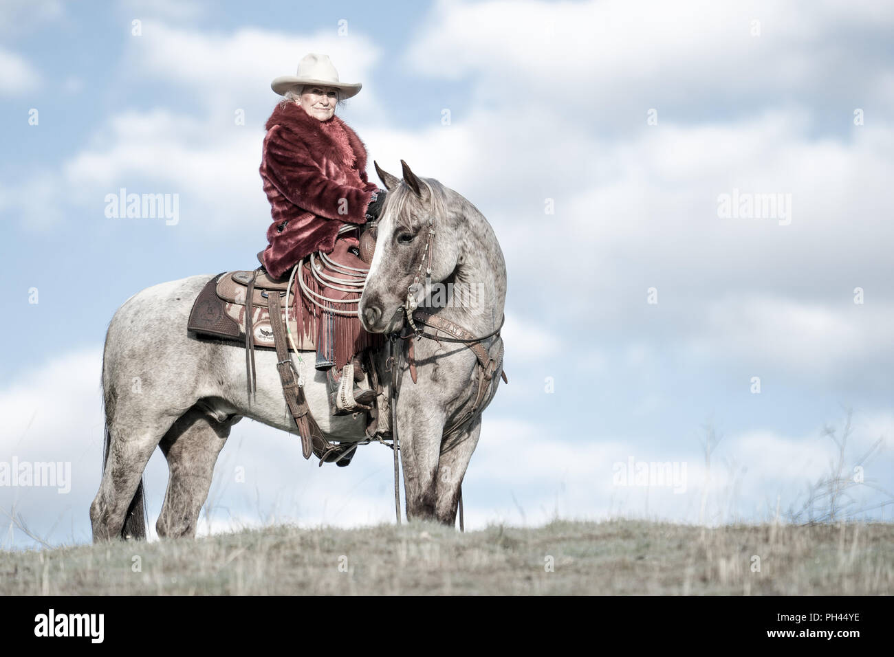 Une seule cavalière dans un manteau de fourrure rouge à califourchon sur son fidèle destrier, l'arpentage de l'étendue de son ranch dans la première lumière du matin Banque D'Images