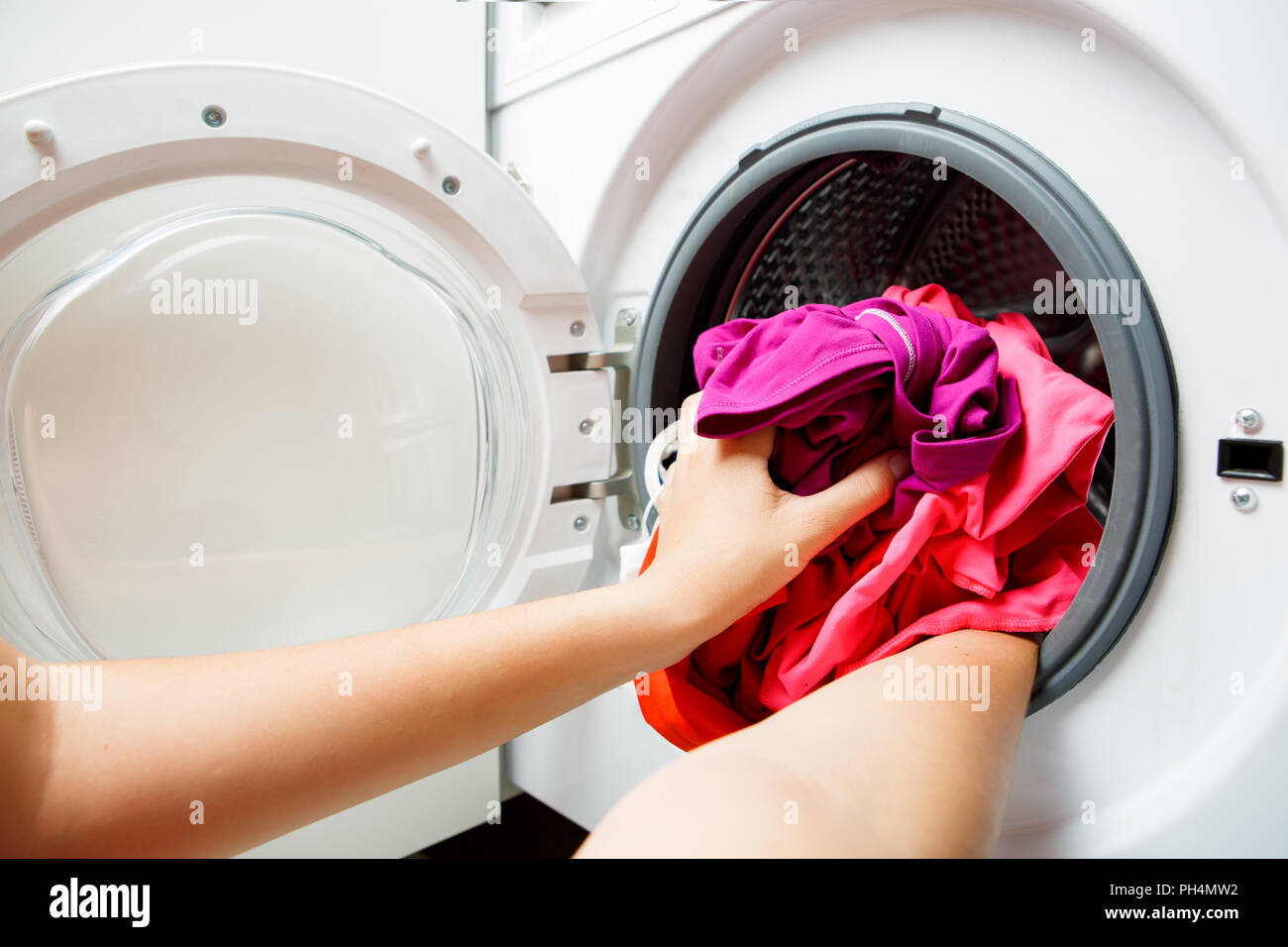La photo d'une femme de pliage mains les choses en rose lave-linge avec porte ouverte Banque D'Images