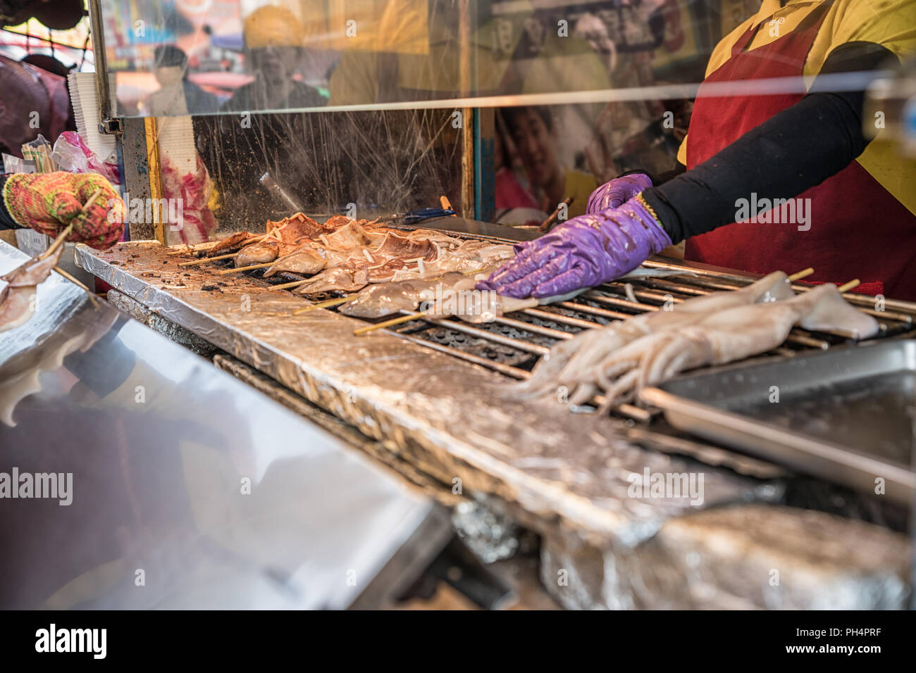 Cuisson du vendeur les aliments sur la cuisinière barbecue. par l'arrière-plan du marché asiatique Banque D'Images