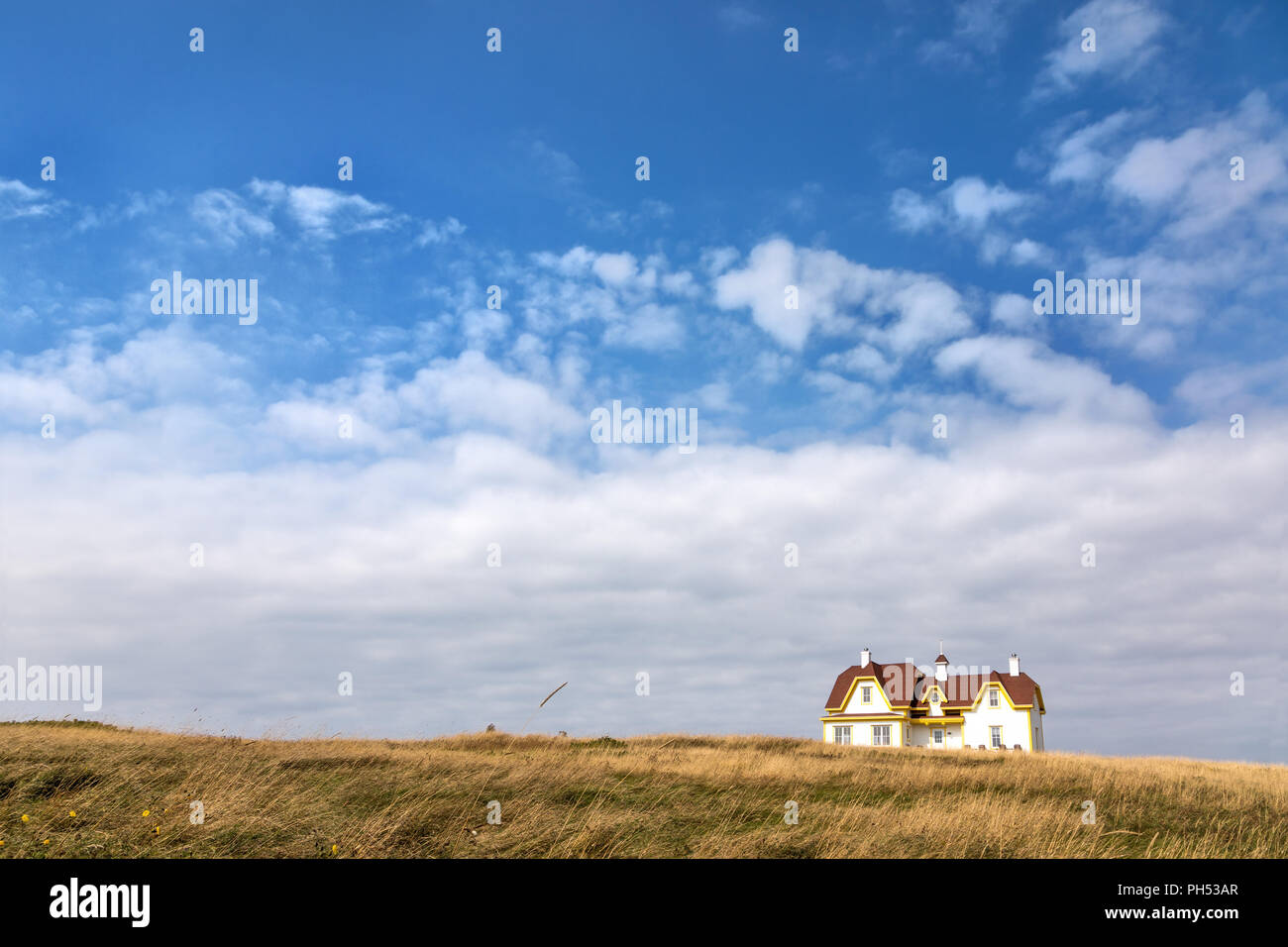 Maison en bois blanc, avec toit en tuiles rouges et jaunes gables, à l'horizon et isolé dans un champ d'herbes sauvages. Cap-aux-Meules, Îles de la Madeleine, Banque D'Images
