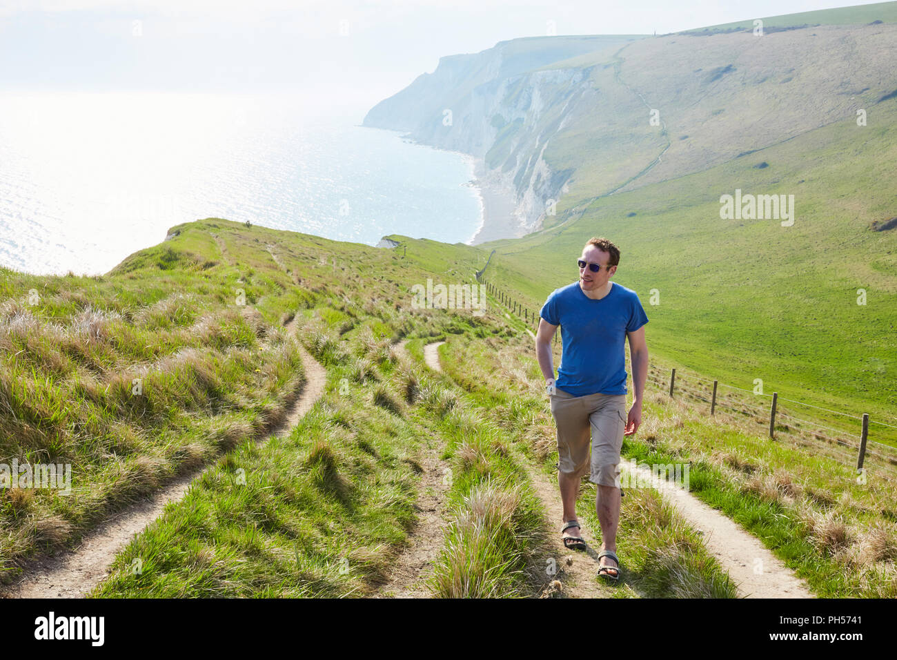 Homme d'âge moyen à la mer pendant qu'il marche en montée vers la caméra sur un banque herbeux le long d'une journée claire, près de Durdle Door sur la côte jurassique Banque D'Images