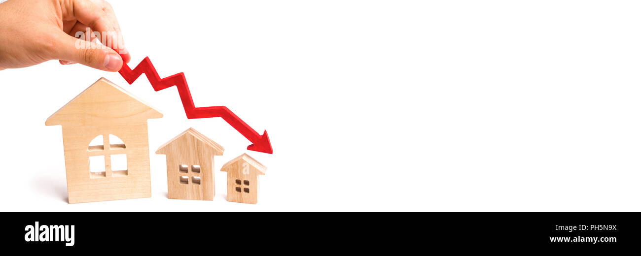 La main est titulaire d'une flèche rouge au-dessus des maisons en bois en bas. Les maisons sont en baisse. Le concept de la baisse de la demande et l'offre sur le marché de l'immobilier Banque D'Images