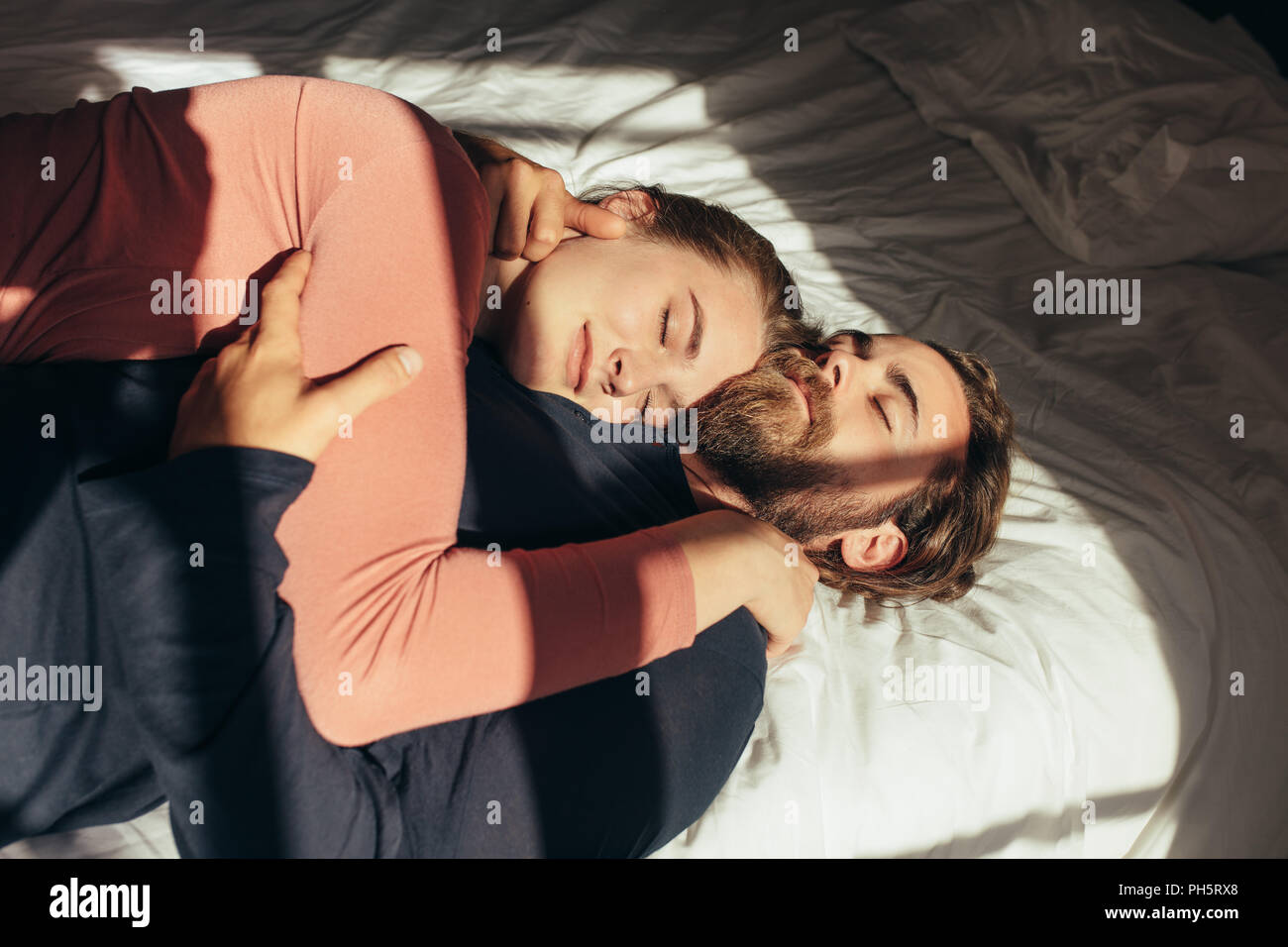 Man sur le bras de son mari avec la lumière du soleil entrant par la fenêtre. Couple relaxing on bed holding les uns les autres avec les yeux fermés. Banque D'Images