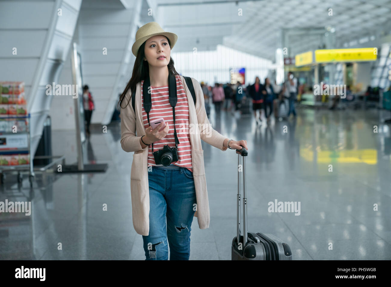 Femme à la recherche de quelque chose en marchant. tenant son téléphone dans la main. par l'arrière-plan de la foule dans l'aéroport. Banque D'Images