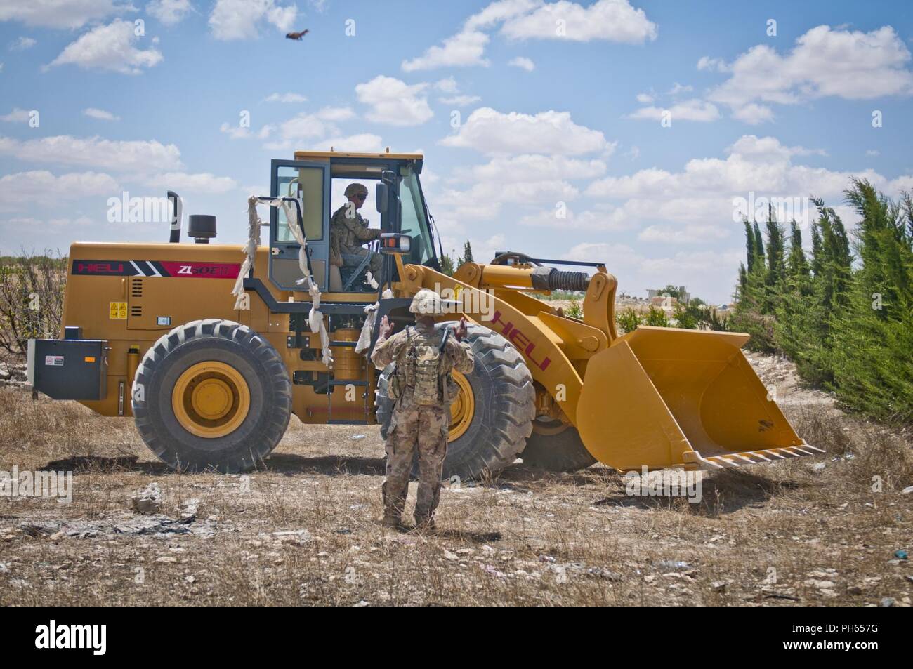 Un soldat américain guides au sol un autre soldat comme il se déplace un chargeur avant en position pour bloquer partiellement près d'une route près de Manbij, Syrie, 20 juin 2018. Le blocus est conçu pour garder les véhicules hors de la ville de Manbij tandis que ceux des États-Unis et de patrouille militaire turc le long de la ligne de démarcation pour assurer la sécurité de la ville. Banque D'Images