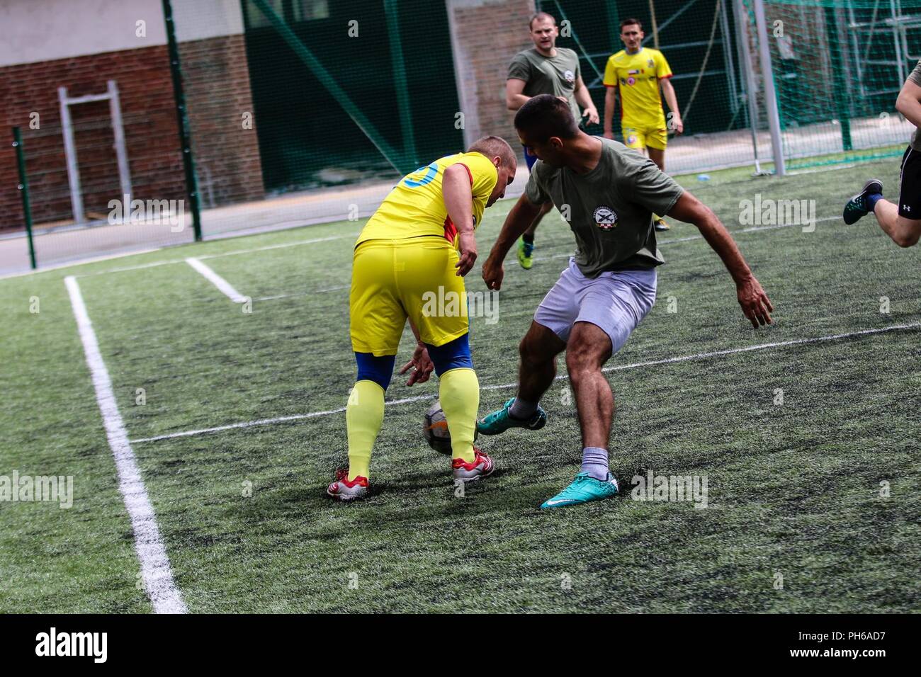 Un soldat de l'armée croate avec fusée d'artillerie "Tempête" de batterie (vert), essaie de frapper un ballon de soccer cours des soldats roumains avec Air Defense Artillery "Scorpions" bleu Batterie (jaune), dans le cadre d'une compétition sportive avec Battle Group Pologne pour célébrer la Journée des Forces armées britanniques à Bemowo Piskie Domaine de formation, la Pologne, le 30 juin 2018. La Pologne est un groupe de combat, unique coalition multinationale d'États-Unis, Royaume-Uni, croate et soldats roumains qui servent avec la 15e Brigade mécanisée polonaise comme une force de dissuasion de l'OTAN à l'appui de l'amélioration de l'avant la Présence. Banque D'Images