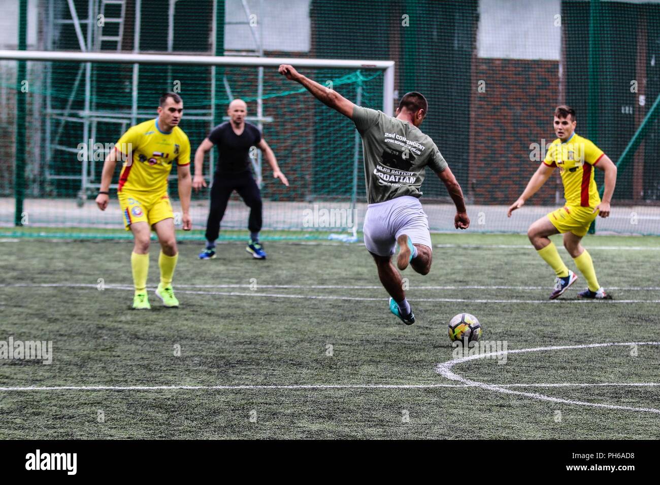 Un soldat de l'armée croate avec fusée d'artillerie "Tempête" de batterie (vert), essaie de frapper un ballon de soccer cours des soldats roumains avec Air Defense Artillery "Scorpions" bleu Batterie (jaune), dans le cadre d'une compétition sportive de groupe de combat avec la Pologne pour célébrer la Journée des Forces armées britanniques à Bemowo Piskie Domaine de formation, la Pologne, le 30 juin 2018. La Pologne est un groupe de combat, unique coalition multinationale d'États-Unis, Royaume-Uni, croate et soldats roumains qui servent avec la 15e Brigade mécanisée polonaise comme une force de dissuasion de l'OTAN à l'appui de l'amélioration de l'avant la Présence. Banque D'Images