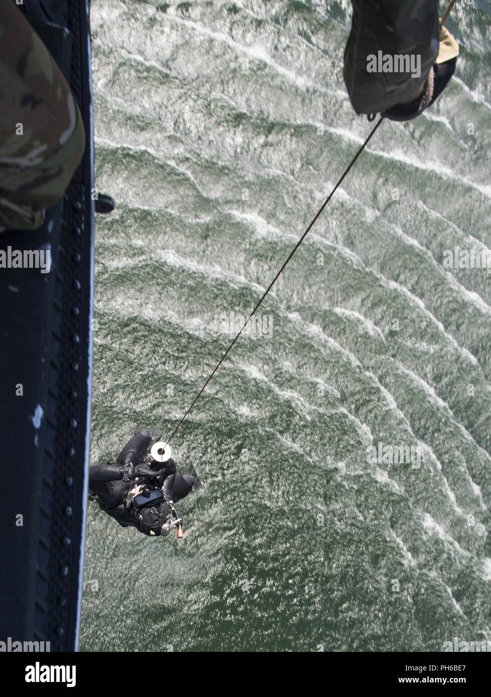 Un Pararescueman s'entraîne avec le 68e Escadron de sauvetage est hissé hors de l'eau dans un UN-H1 Huey à Long Lake, Washington, le 26 juin 2018. Le Huey a commencé à être utilisé par l'Armée de l'air en 1970 comme un actif de recherche et de sauvetage. Les missions de la cellule de l'élargi pour inclure la sécurité des missiles, visiteur de marque, l'École de survie et de test support. Banque D'Images