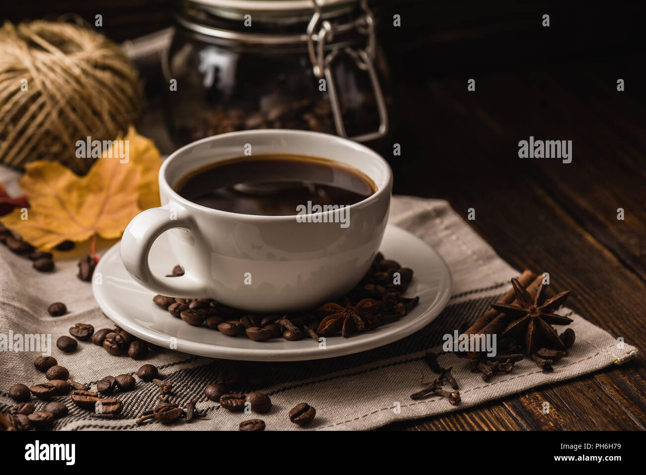 Tasse de café blanc avec diverses épices, les haricots et les feuilles d'automne jaune foncé sur fond de bois Banque D'Images