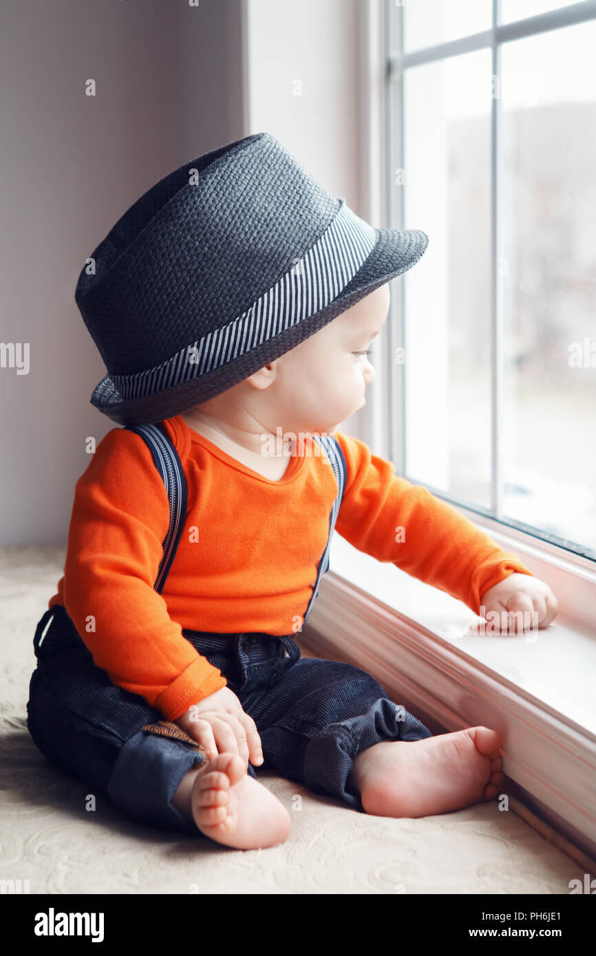 Portrait of cute adorable bébé garçon caucasien élégant avec chapeau,  chemise orange onesie, jeans avec bretelles nu assis sur le rebord de la  fenêtre à l'écart, n Photo Stock - Alamy