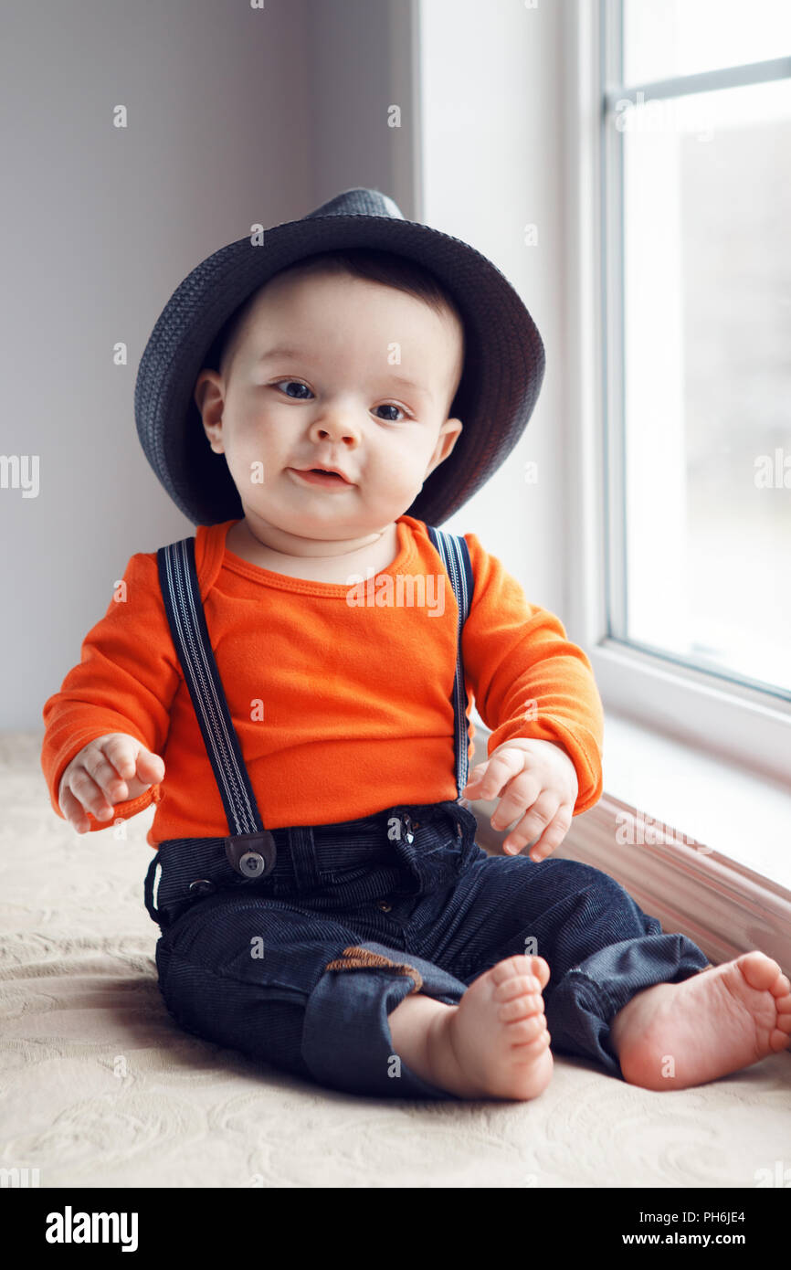 Portrait of cute adorable bébé caucasien élégant garçon avec des yeux noirs  hat, orange shirt onesie, jeans avec bretelles nu assis on windowsill Photo  Stock - Alamy