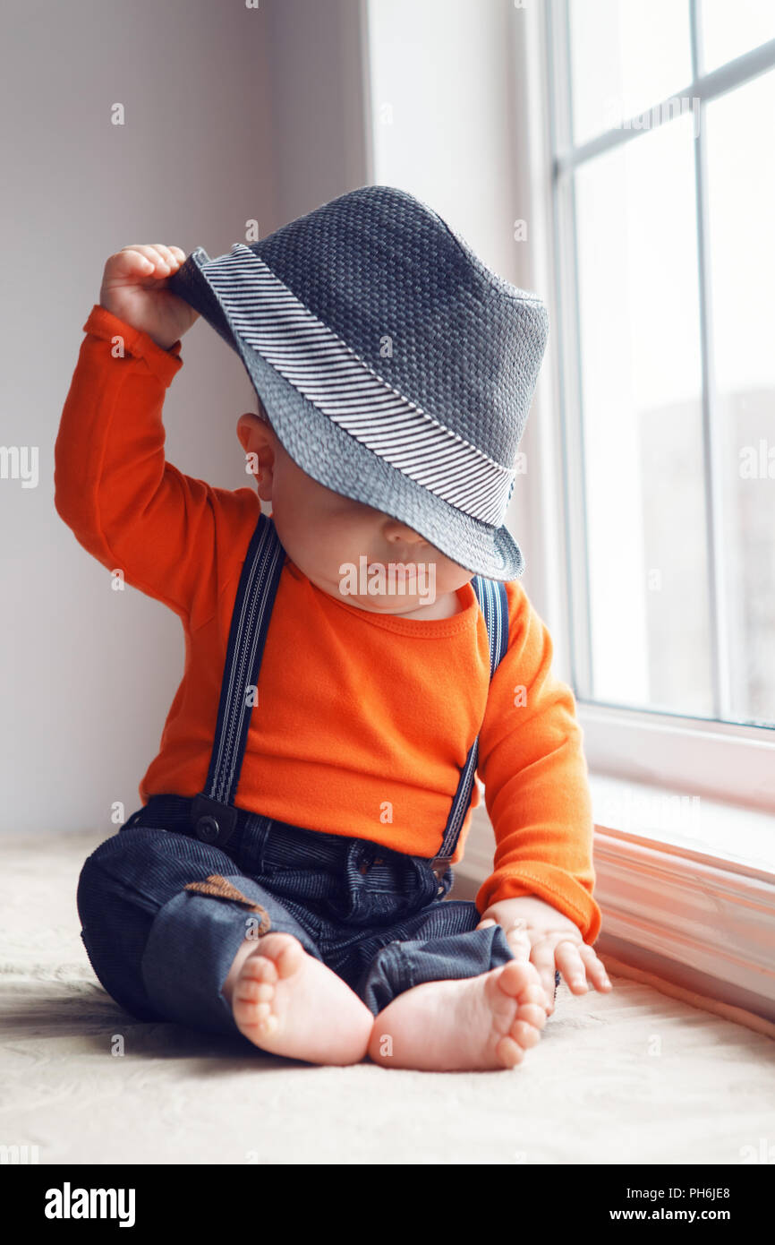 Portrait of cute adorable bébé garçon caucasien élégant en orange shirt  onesie, jeans avec bretelles nu assis sur le rebord de son chapeau ,  décollage Photo Stock - Alamy