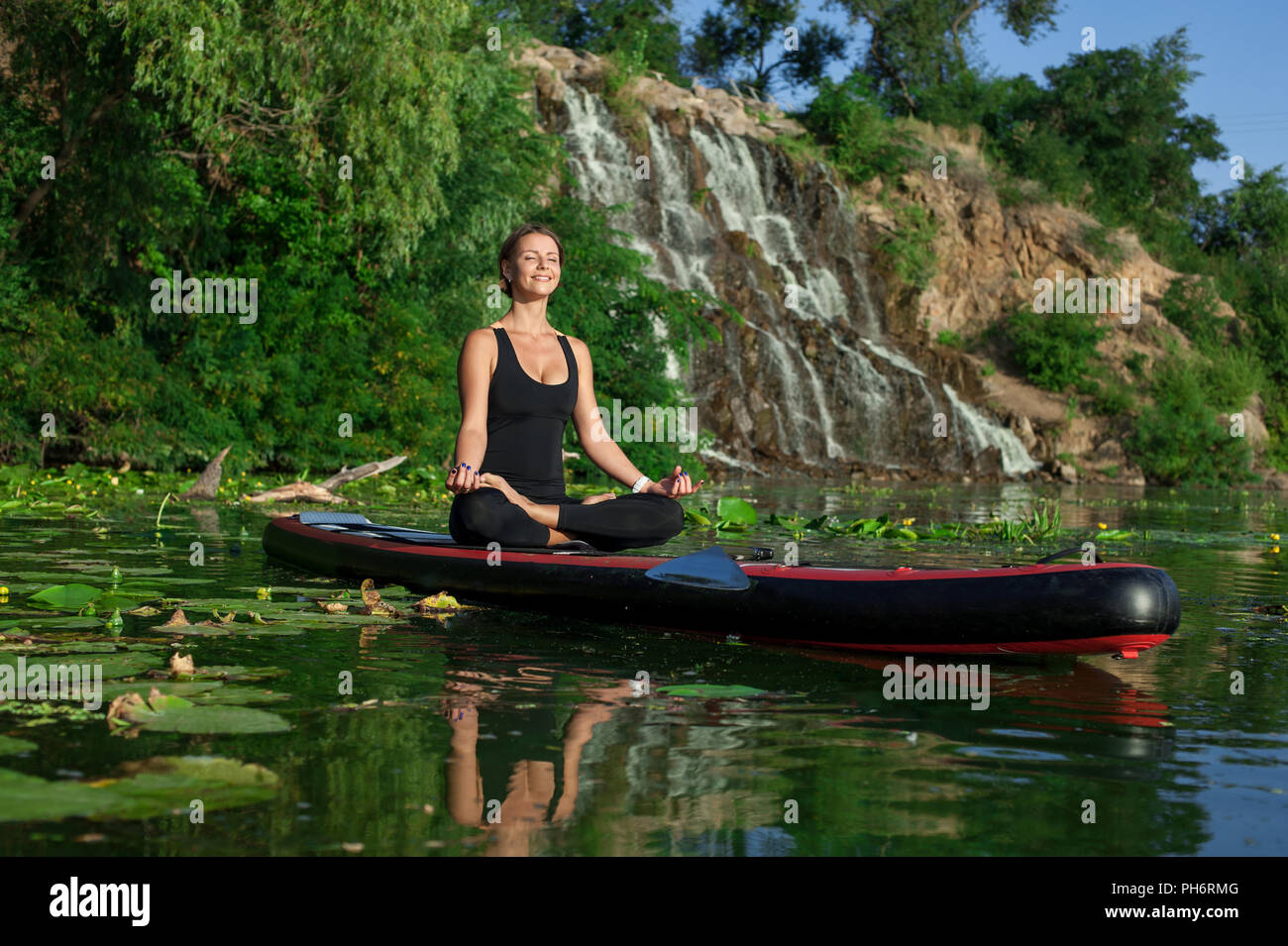 Belle jeune femme méditant sur une rivière à paddleboarding SUP Banque D'Images